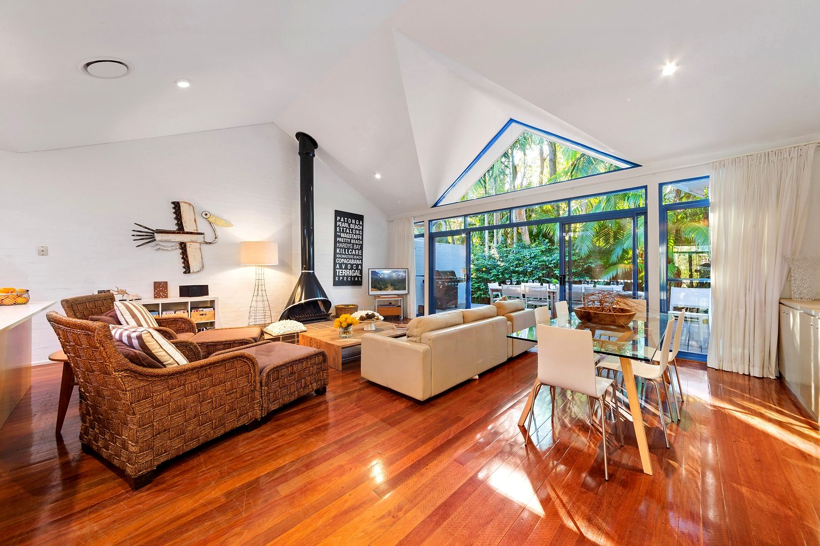 Open-plan living room at Sails Pearl Beach with lofted ceiling, fireplace and glass doors to the deck