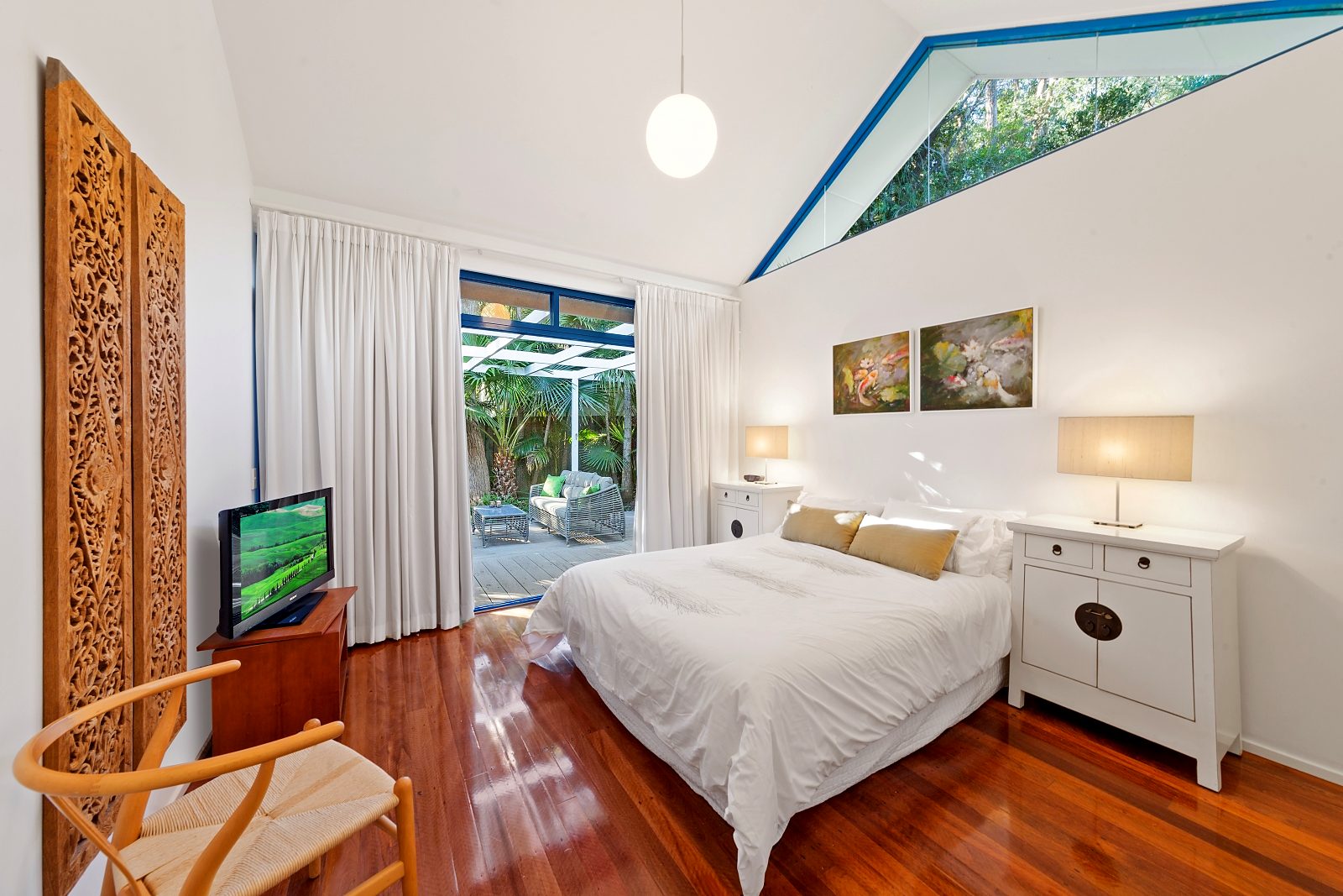 Main bedroom at Sails Pearl Beach: queen bed, carved timber screen and doors to the deck