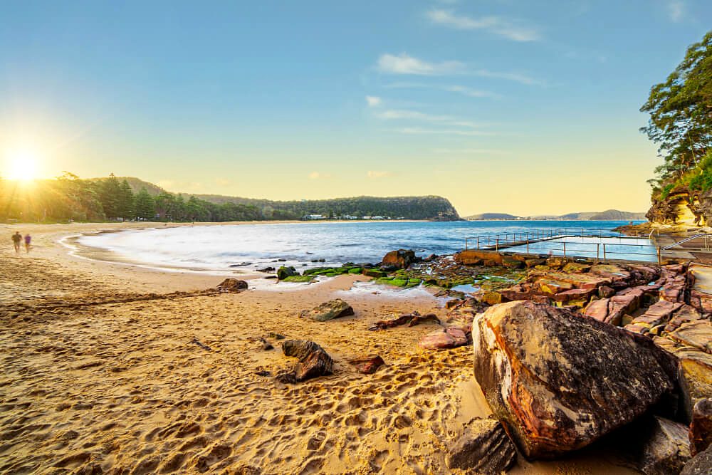 The ocean rock pool at the southern end of Pearl Beach at sunset, sandstone rocks in the foreground